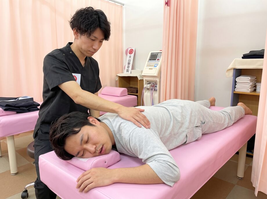 施術ベッドでうつ伏せになり、背中をほぐされながら眠っている男性
